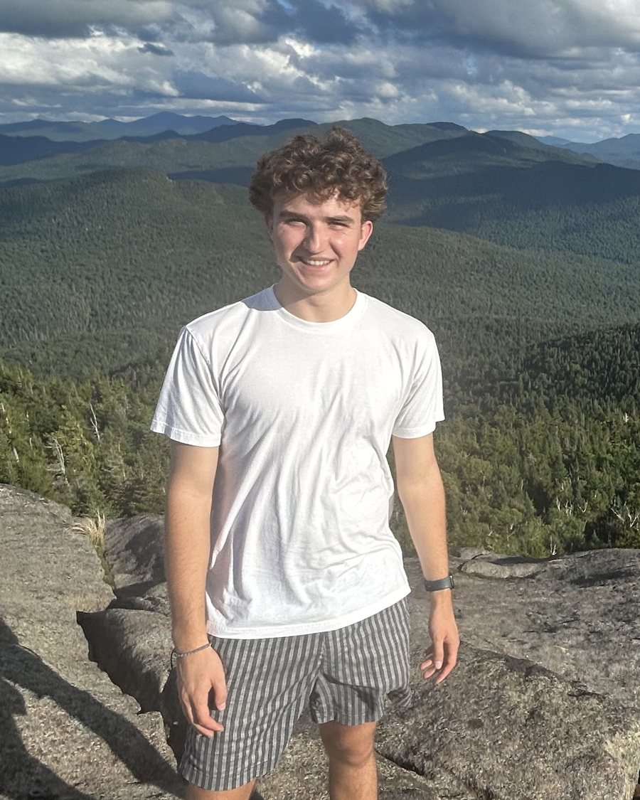 Nathaniel Corey standing on a rock ledge above a forested valley in the Adirondacks.