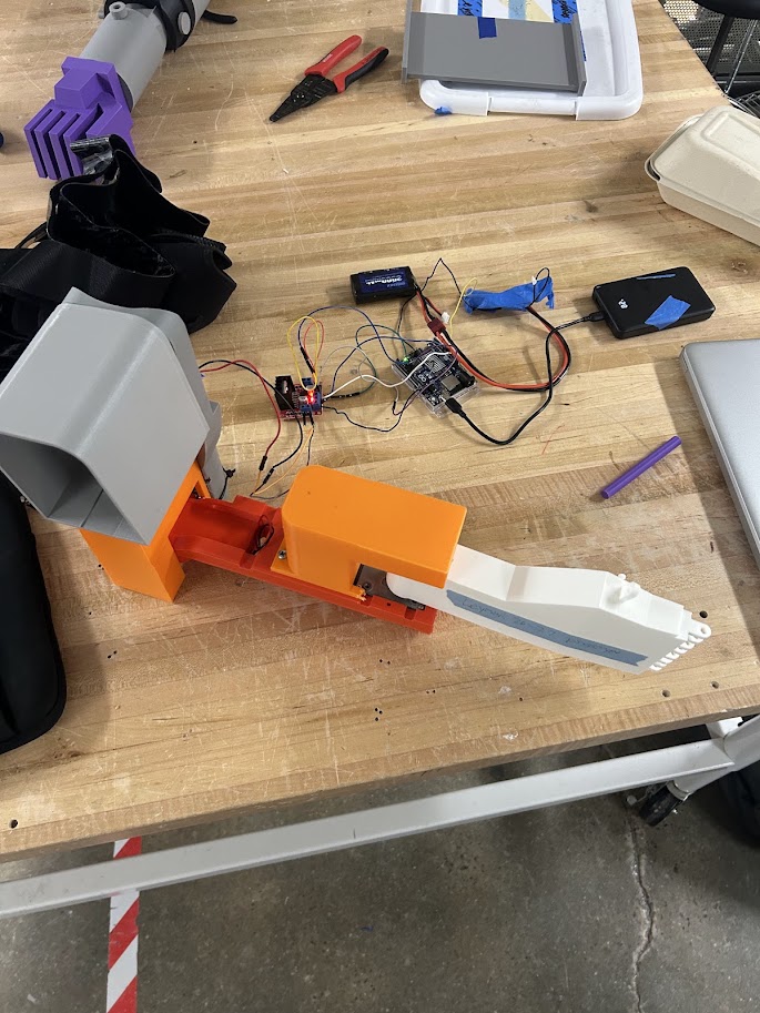 The prosthetic arm prototype: an Arduino and driver electronics in a 3D-printed orange housing above a geared motor, wired to the forearm assembly.