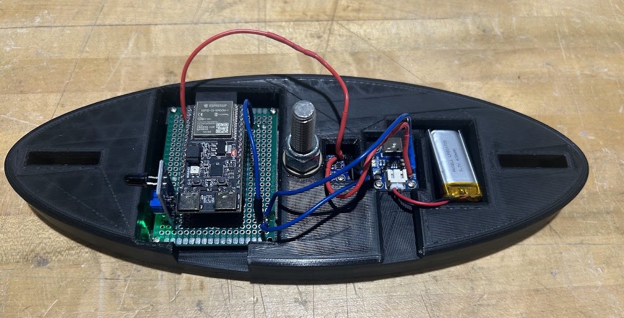 The assembled rotor: an elliptical 3D-printed body with recessed bays holding an ESP32-C6 and IR sensor on a soldered protoboard, a center spindle bolt, a buck converter, a battery charger board, and a 400 mAh LiPo battery, wired together.